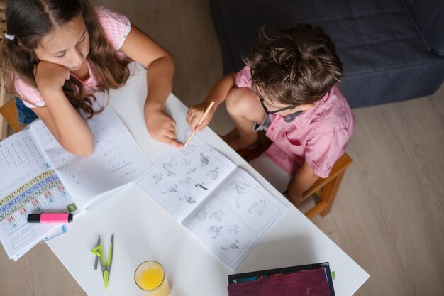 Foto linda garota e menino de óculos, estudando em casa, fazer lição de casa. irmã ajude irmão mais novo. irmãos. escrevendo. laptop na mesa. conceito de educação remota. quarentena. de volta ao conceito de escola. vista do topo.