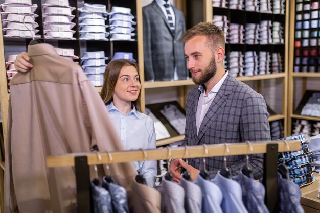 Linda garota elegante apresenta uma camisa de estilo de negócios para um homem confiante em uma loja de roupas masculinas