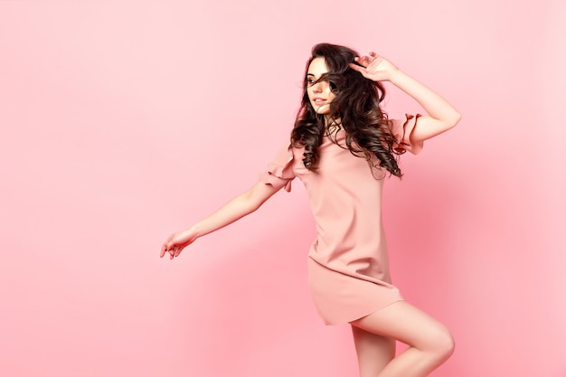 Linda garota elegante com cabelo longo cacheado em um vestido rosa no estúdio em um fundo rosa.