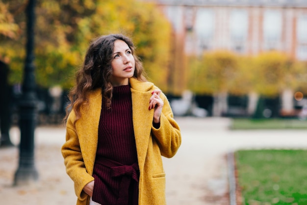 Linda garota elegante com um casaco amarelo caminha pelas ruas de Paris