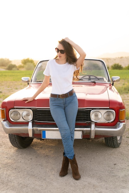 Linda garota em estilo retrô posando perto de carro conversível vermelho vintage