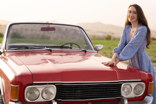 Linda garota em estilo retrô posando perto de carro conversível vermelho vintage