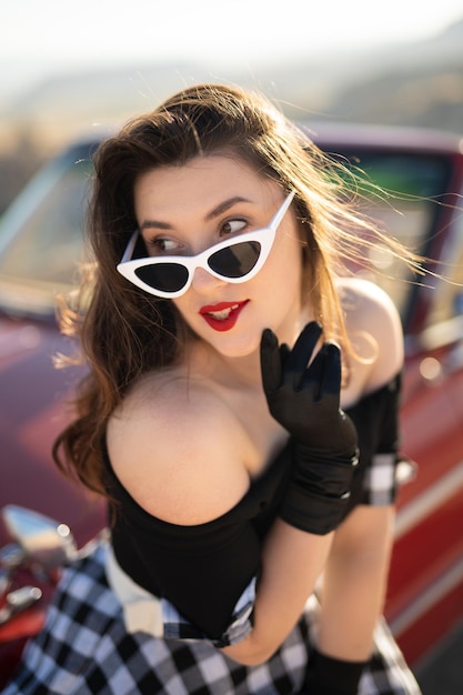 Linda garota em estilo retrô posando perto de carro conversível vermelho vintage