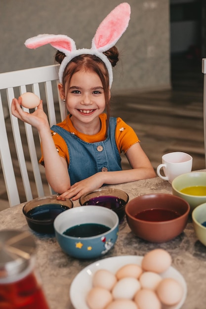 Linda garota em orelhas de coelho pintar ovos de páscoa