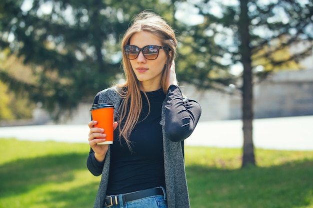 Linda garota em pé na rua com café e copos.