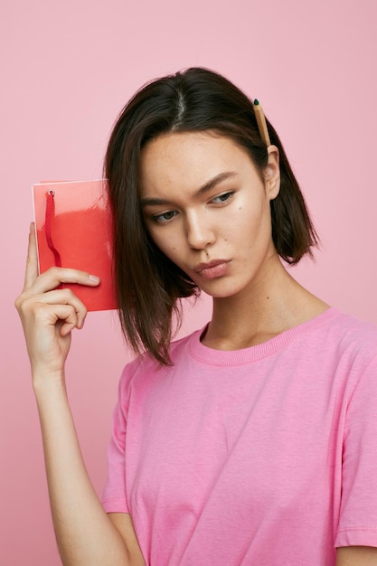 Linda garota em um caderno vermelho de camiseta rosa e caneta Estilo de vida inalterado