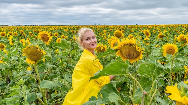 Linda garota em um campo de girassol em uma camisa amarela no verão no calor do dia