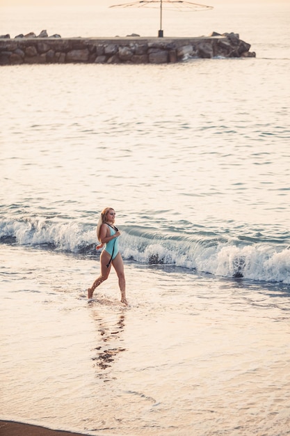 Linda garota em um maiô azul e um chapéu em uma praia de areia no mar sob o sol do sol