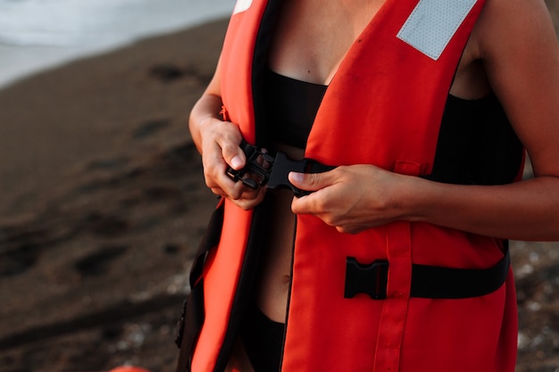 Foto linda garota em um maiô preto e um colete salva-vidas na praia