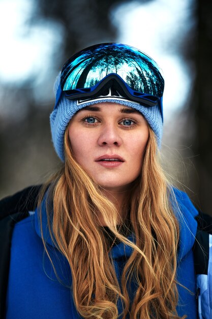 Linda garota em um terno de esqui azul e capacete. Na cabeça estão óculos para snowboard. Paisagem montanhosa coberta de neve. Retrato de um piloto. É assim que se parece a felicidade.