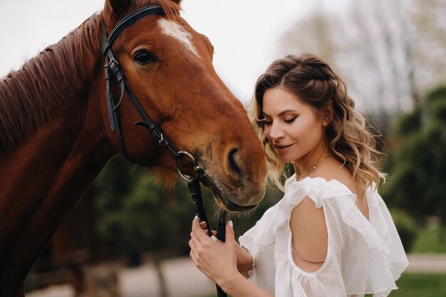 Linda garota em um vestido branco ao lado de um cavalo em um antigo rancho