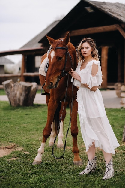 Linda garota em um vestido branco ao lado de um cavalo em um antigo rancho