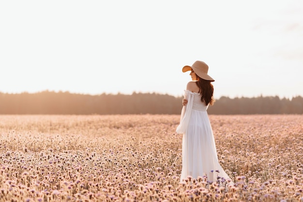 Linda garota em um vestido branco em um campo de lavanda ao pôr do sol.