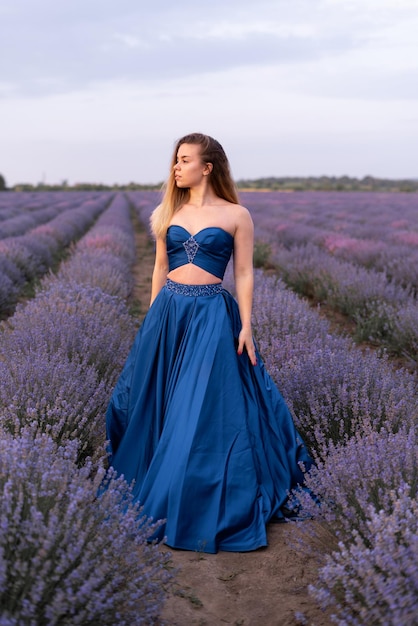 Linda garota em um vestido de noiva azul fica em um campo de lavanda.