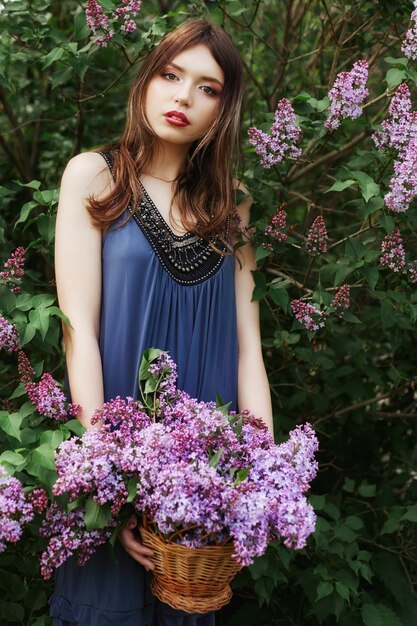 Linda garota em um vestido se passando perto de um arbusto de lilases em um dia de verão, flores roxas no parque. Retrato de primavera de uma menina na natureza ao sol