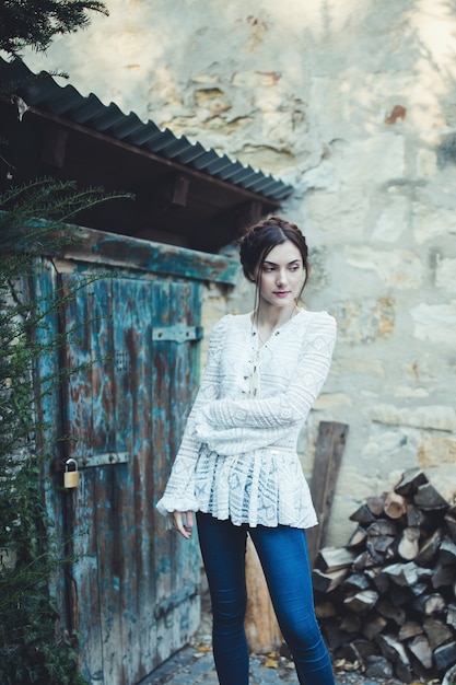 Linda garota em uma blusa de renda branca e calça jeans perto da casa do fazendeiro