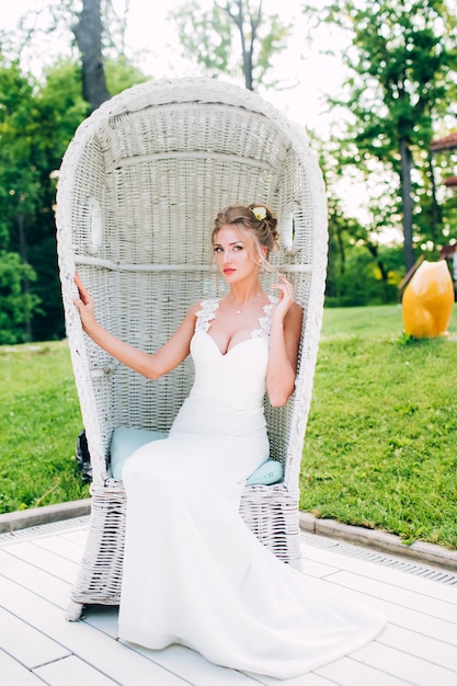 Linda garota em uma cadeira branca na natureza. Loira de vestido com decote profundo.