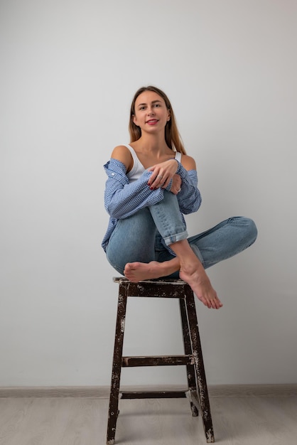 Linda garota em uma camiseta branca, jeans azul, sentada em uma cadeira, sorrindo e posando