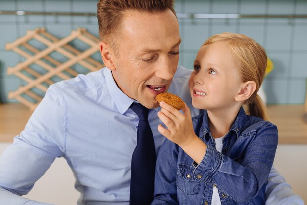 Linda garota encantada segurando um biscoito e dando ao pai