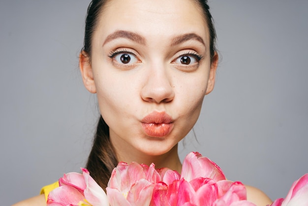 Linda garota engraçada segurando flores cor de rosa olhando para a câmera e posando