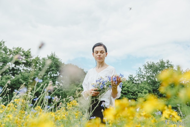 Linda garota entre o campo de verão com flores silvestres