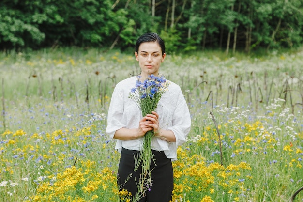 Linda garota entre o campo de verão com flores silvestres