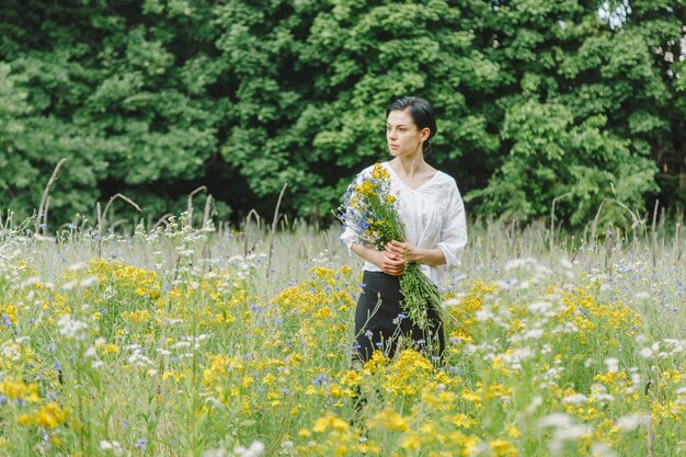 Linda garota entre o campo de verão com flores silvestres