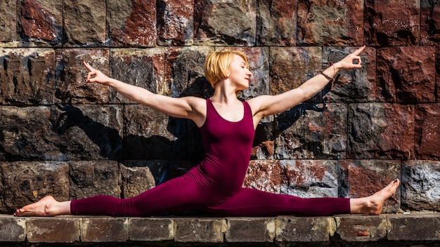 Linda garota envolvida em yoga no fundo de um muro de pedra