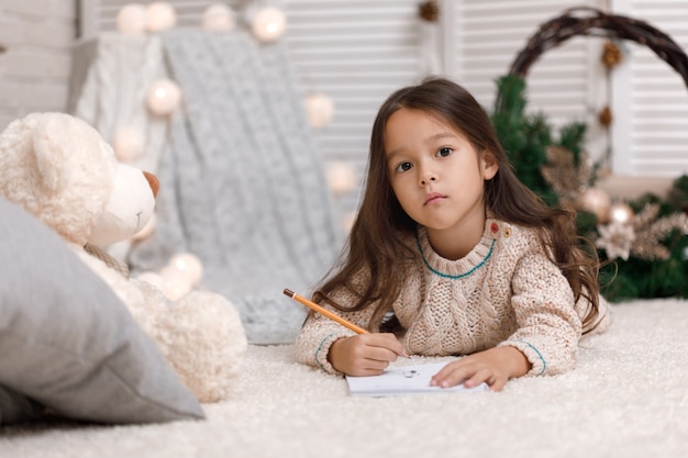 Linda garota escrevendo uma carta para o Papai Noel em casa