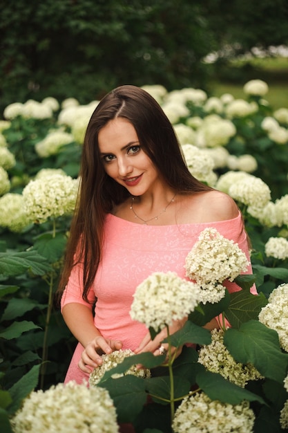 Linda garota está em arbustos de flores de hortênsia no jardim do sol. flores florescendo nas ruas da cidade.