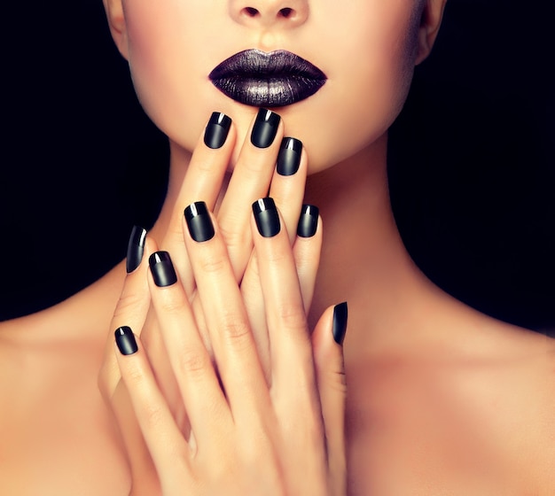 Foto linda garota está mostrando manicure preta nas unhas na frente dos lábios bem formados pintados de preto. detalhe do close up. maquiagem, cosmética e manicure.