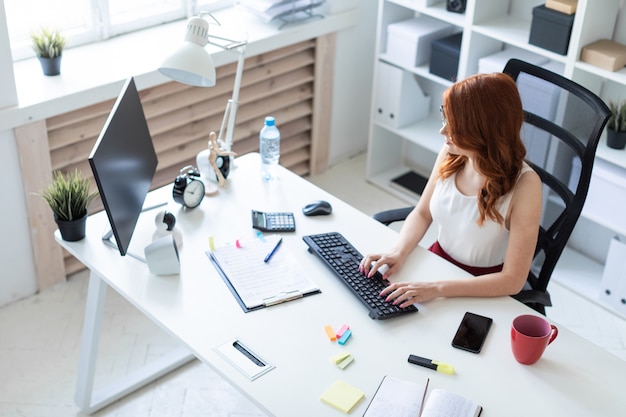 Linda garota está sentado a mesa no escritório e digitando no teclado.