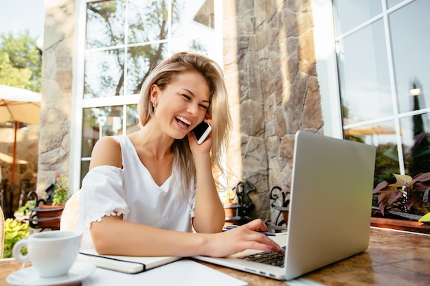 Linda garota falando no telefone enquanto estiver trabalhando com o laptop