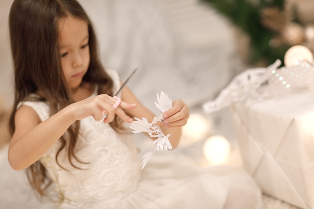Linda garota fazendo flocos de neve de papel para decorar o Natal