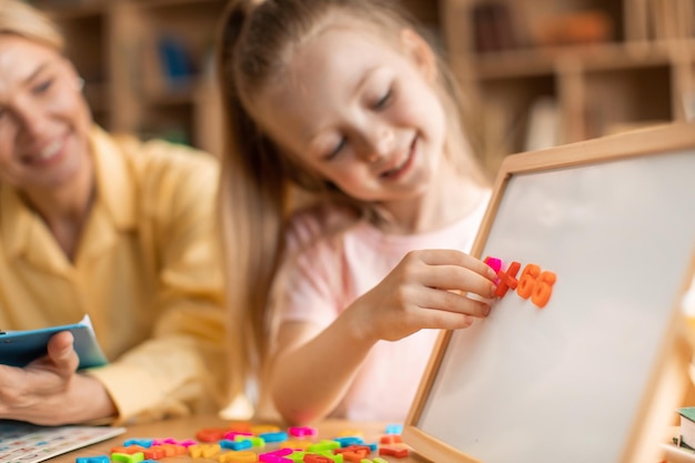 Linda garota feliz aprendendo o alfabeto alegre especialista em desenvolvimento infantil trabalhando com criança sorridente