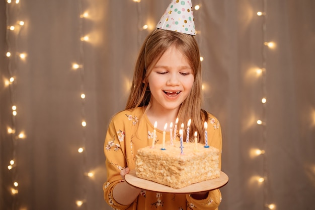 linda garota feliz com bolo de aniversário. tradição de fazer um pedido e apagar o fogo na festa