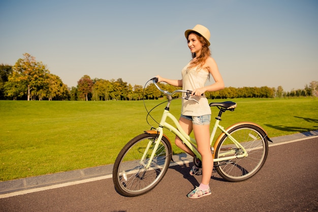 Linda garota feliz com uma bicicleta caminhando no parque