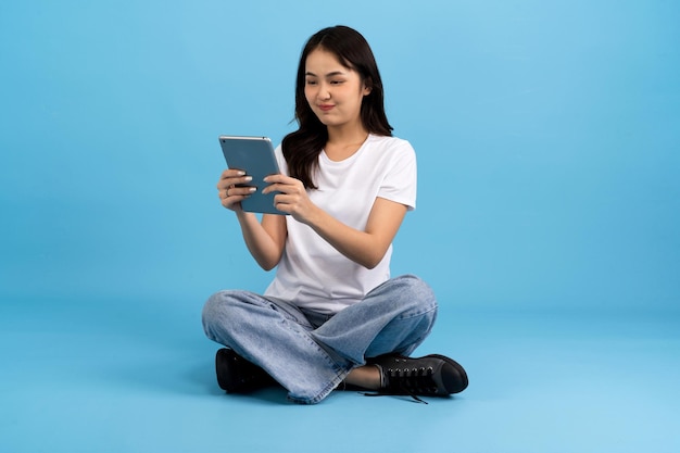 Linda garota feliz segurando o computador tablet sentado no fundo azul