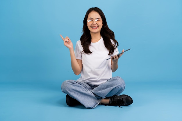 Linda garota feliz segurando o computador tablet sentado no fundo azul