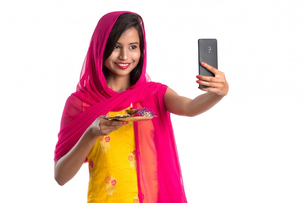 Linda garota feliz tomando selfie com pooja thali usando um telefone celular ou smartphone