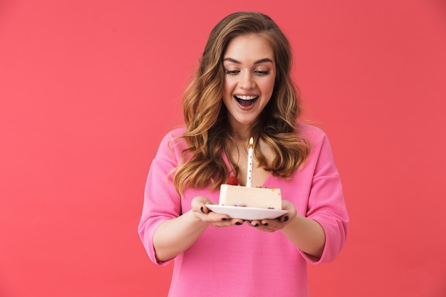 Linda garota feliz, vestindo roupas casuais, em pé, isolada na parede rosa, comemorando aniversário com bolo