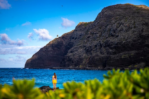 linda garota fica nas rochas admirando o pôr do sol sobre o farol de makapu'u em oahu, havaí