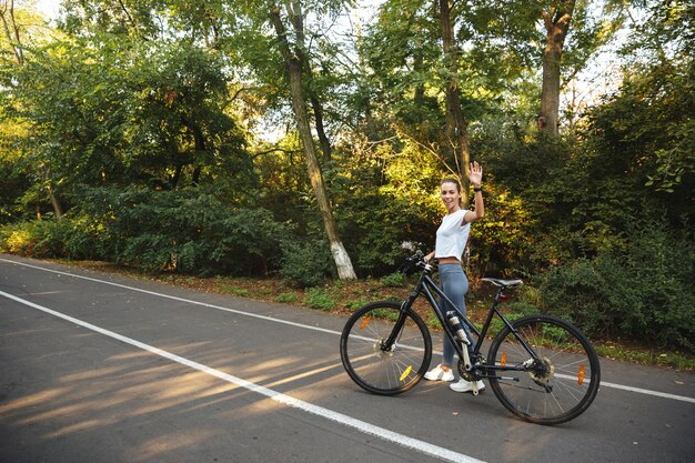 Linda garota fitness caminhando de bicicleta na estrada do parque