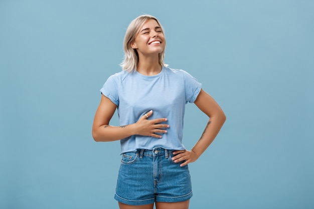 Foto linda garota gosta de comer depois do treino, ficar satisfeita e recheada depois do jantar. retrato de uma jovem loira atraente e satisfeita tocando a barriga, levantando a cabeça com um largo sorriso