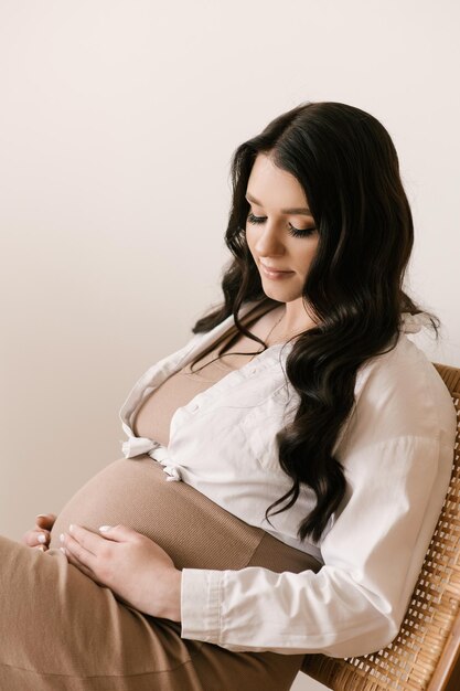 Linda garota grávida com cachos em um vestido em um estúdio brilhante com um interior elegante o conceito de uma gravidez feliz e família