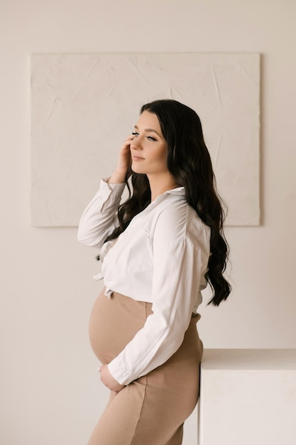 Linda garota grávida com cachos em um vestido em um estúdio brilhante com um interior elegante o conceito de uma gravidez feliz e família