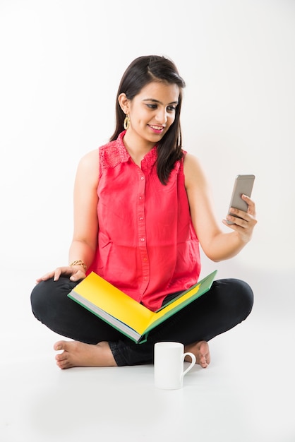 Linda garota indiana asiática usando um telefone Cel ou smartphone enquanto estuda, contra um fundo branco