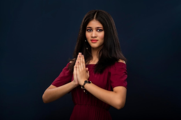Linda garota indiana com expressão de boas-vindas ou convidando ou cumprimentando Namaste em um fundo cinza