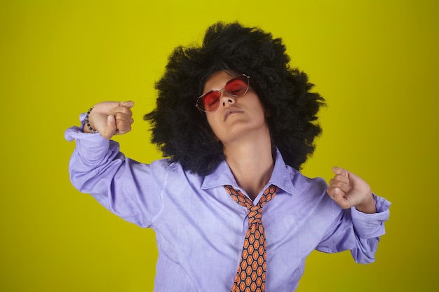 Linda garota indiana com penteado afro encaracolado e roupas masculinas acordando e se espreguiçando na parede amarela