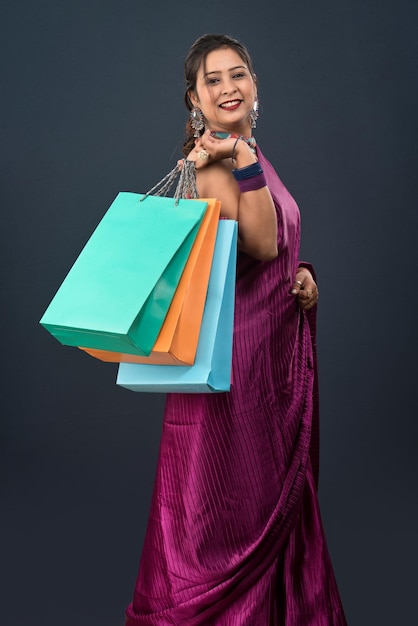 Linda garota indiana segurando e posando com sacolas de compras em um fundo cinza